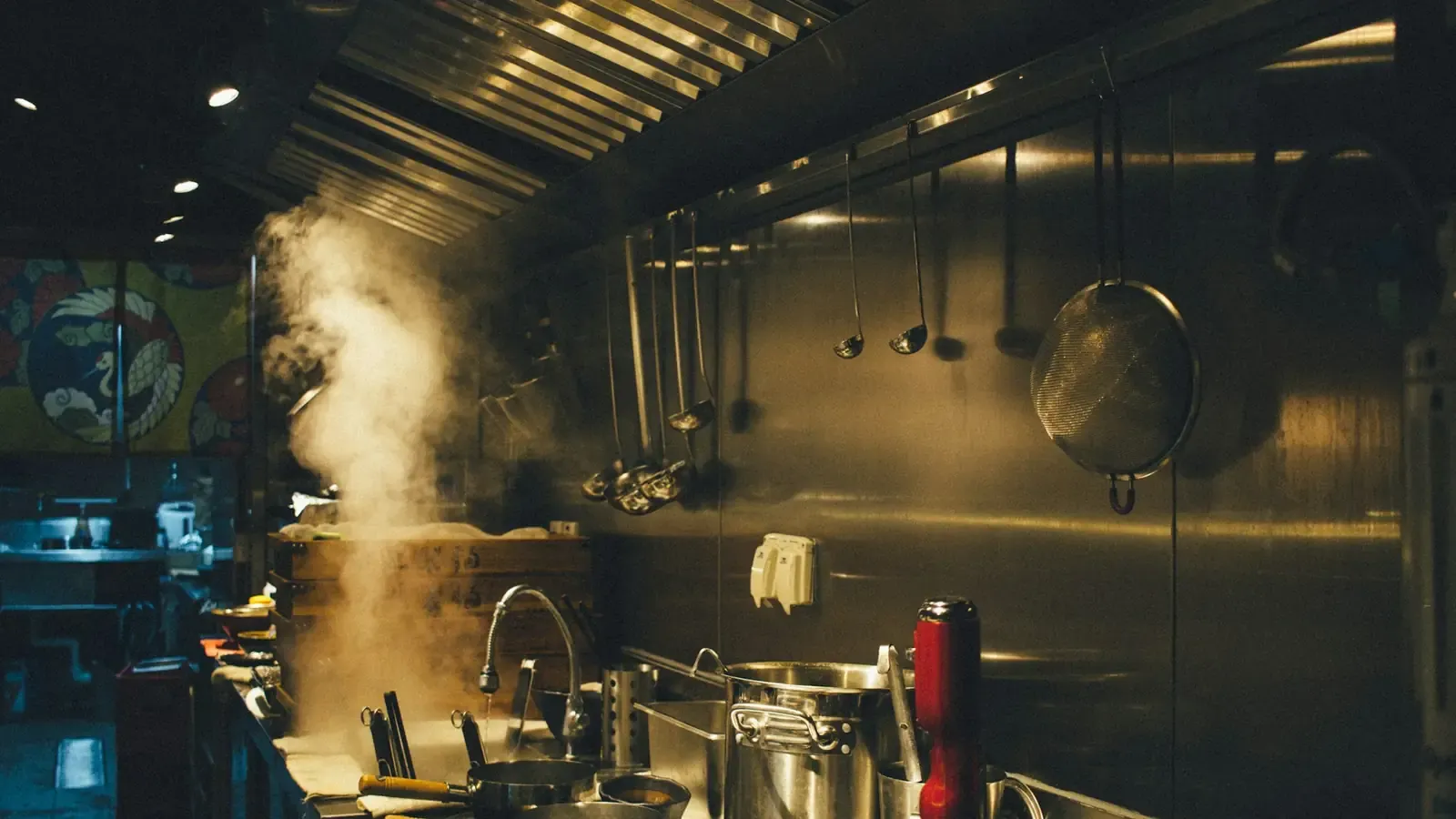 Professionele keuken met stomende pannen op het fornuis onder een roestvrijstalen afzuigkap